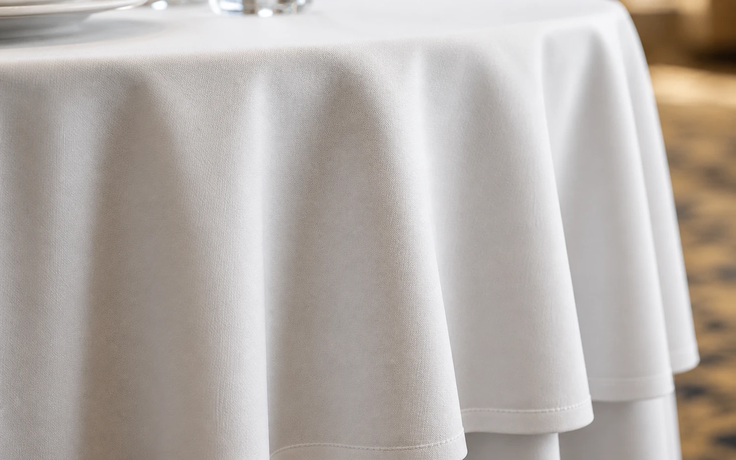 Close-up of white hotel tablecloth fabric draping over a banquet table edge